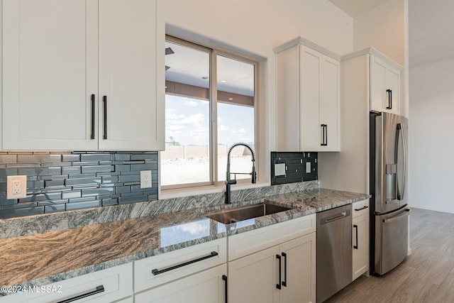 kitchen with light stone countertops, appliances with stainless steel finishes, light hardwood / wood-style floors, sink, and white cabinetry