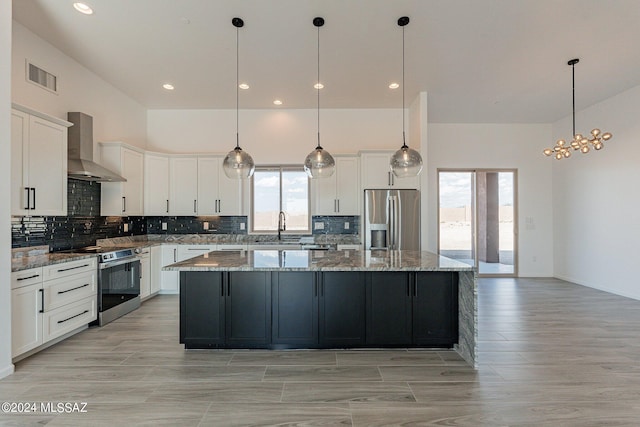 kitchen featuring appliances with stainless steel finishes, a spacious island, hanging light fixtures, and wall chimney range hood