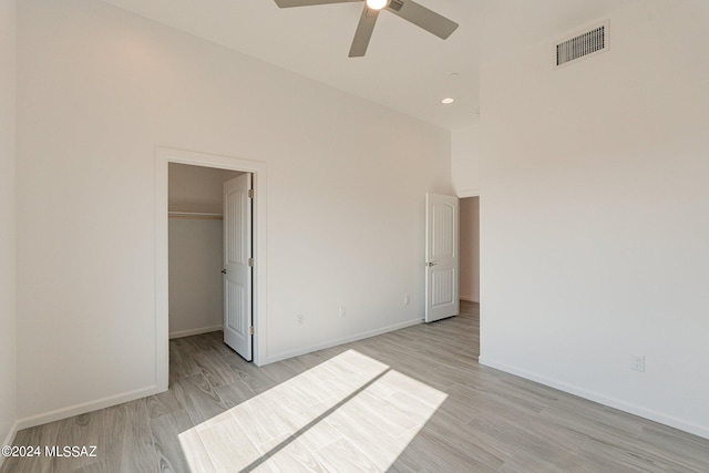 unfurnished bedroom with a high ceiling, ceiling fan, a closet, a walk in closet, and light hardwood / wood-style floors