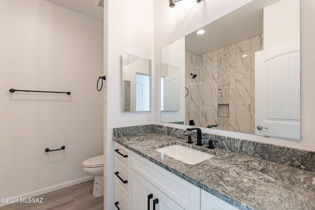 bathroom with tiled shower, wood-type flooring, toilet, and vanity