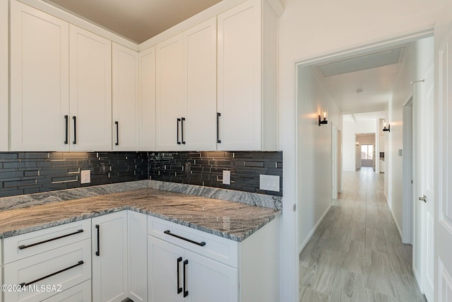 kitchen with stone countertops, white cabinets, light hardwood / wood-style floors, and tasteful backsplash