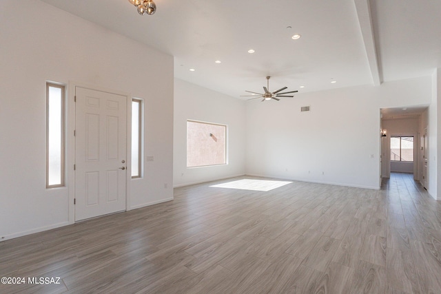 unfurnished living room featuring ceiling fan, light wood-type flooring, and beam ceiling