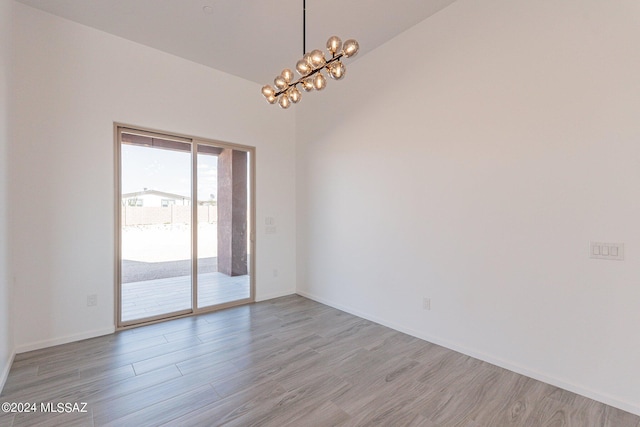 spare room featuring lofted ceiling, a chandelier, and light hardwood / wood-style floors