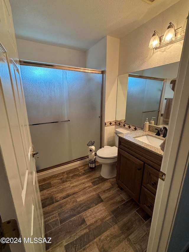 bathroom with a textured ceiling, toilet, wood-type flooring, a shower with shower door, and vanity