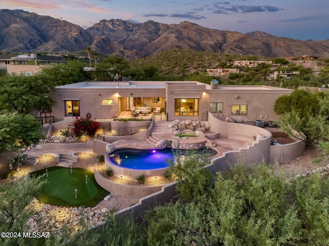 back house at dusk with a patio, a mountain view, and a pool with hot tub