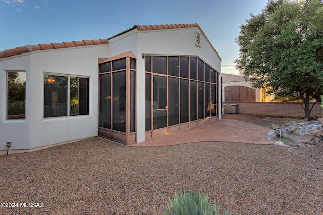 back house at dusk with a sunroom and a patio