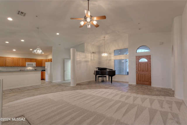 foyer entrance featuring ceiling fan with notable chandelier, light colored carpet, and high vaulted ceiling