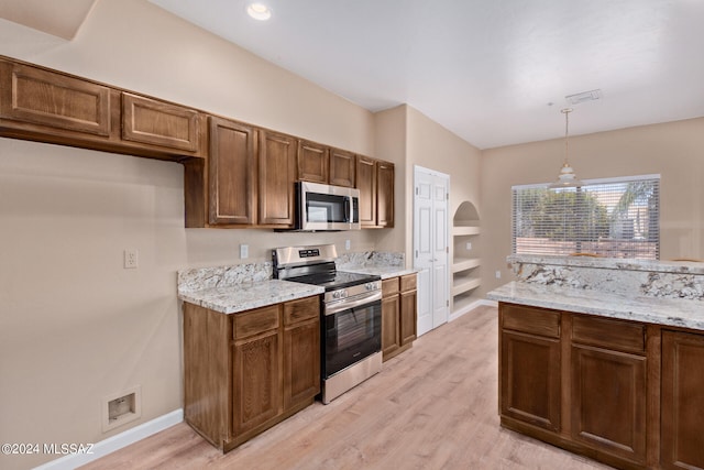 kitchen with light wood-type flooring, appliances with stainless steel finishes, light stone countertops, and pendant lighting