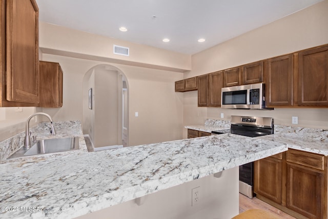 kitchen with light stone countertops, kitchen peninsula, stainless steel appliances, and sink