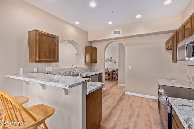 kitchen featuring a kitchen breakfast bar, light hardwood / wood-style flooring, kitchen peninsula, sink, and stainless steel appliances