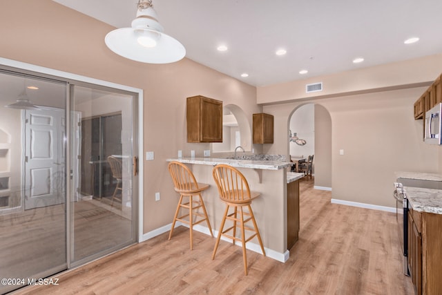 kitchen featuring light hardwood / wood-style flooring, stainless steel electric stove, light stone counters, kitchen peninsula, and a breakfast bar area