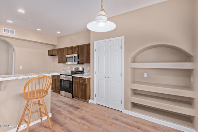 kitchen featuring pendant lighting, stainless steel appliances, light stone countertops, and light wood-type flooring