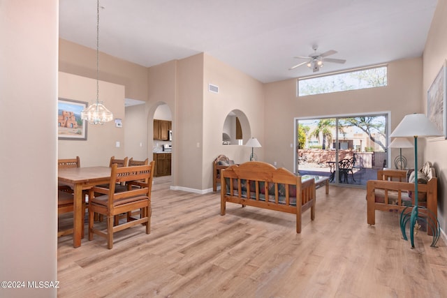 living room with light hardwood / wood-style flooring, a towering ceiling, and ceiling fan with notable chandelier