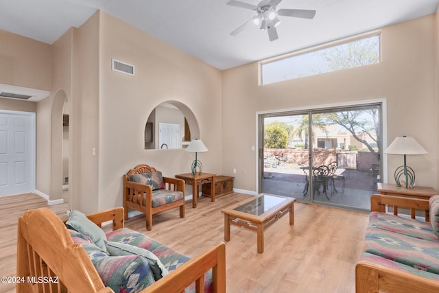 living room with a towering ceiling, light hardwood / wood-style flooring, and ceiling fan