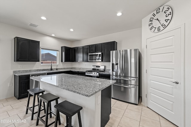 kitchen with sink, light stone countertops, appliances with stainless steel finishes, a kitchen island, and a breakfast bar area