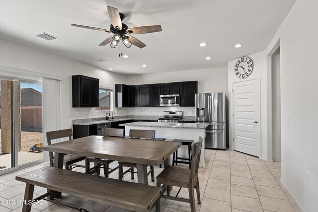 kitchen with appliances with stainless steel finishes, light stone counters, ceiling fan, a center island, and light tile patterned flooring