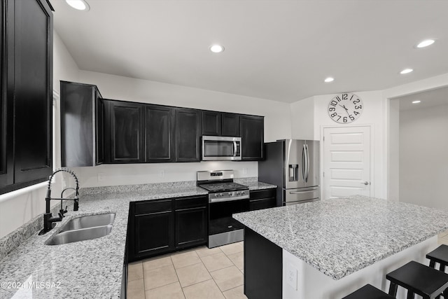 kitchen with a sink, a breakfast bar area, dark cabinetry, appliances with stainless steel finishes, and a center island