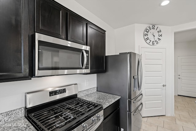 kitchen featuring stainless steel appliances, recessed lighting, dark cabinetry, light stone counters, and light tile patterned floors