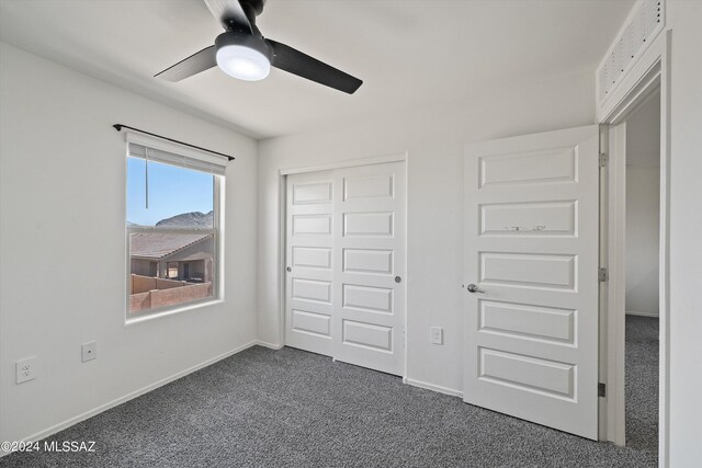 unfurnished bedroom with ceiling fan and dark colored carpet