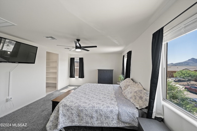 carpeted bedroom with a mountain view, a walk in closet, multiple windows, and ceiling fan