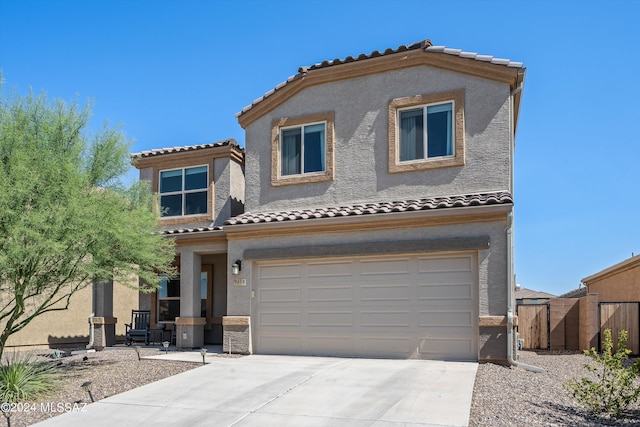mediterranean / spanish-style house featuring a tile roof, concrete driveway, stucco siding, fence, and a garage