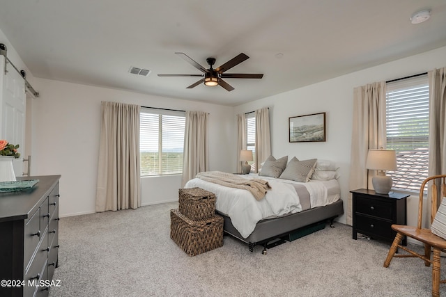 bedroom featuring light colored carpet, ceiling fan, a barn door, and multiple windows