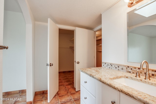 bathroom with backsplash, tile patterned flooring, vanity, and a skylight