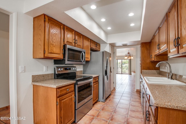 kitchen with light tile patterned flooring, sink, appliances with stainless steel finishes, a notable chandelier, and light stone countertops