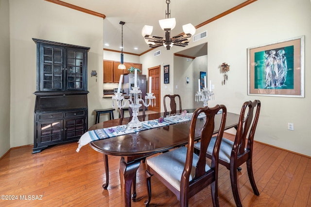 dining room featuring light wood-type flooring, ornamental molding, and an inviting chandelier