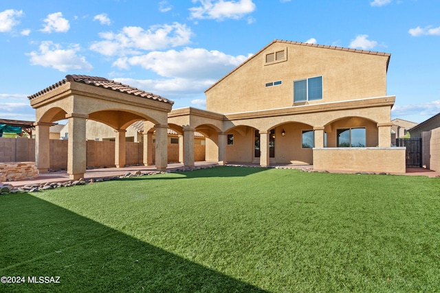 rear view of house with fence, a patio area, a tiled roof, a lawn, and stucco siding
