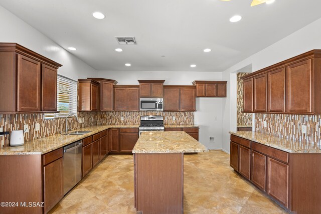 kitchen featuring backsplash, light stone countertops, stainless steel appliances, sink, and a kitchen island