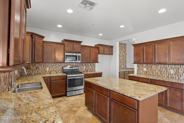 kitchen featuring backsplash, stainless steel appliances, a center island, light stone countertops, and sink