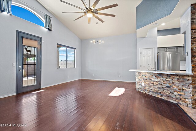 unfurnished living room with ceiling fan with notable chandelier, dark hardwood / wood-style floors, and high vaulted ceiling