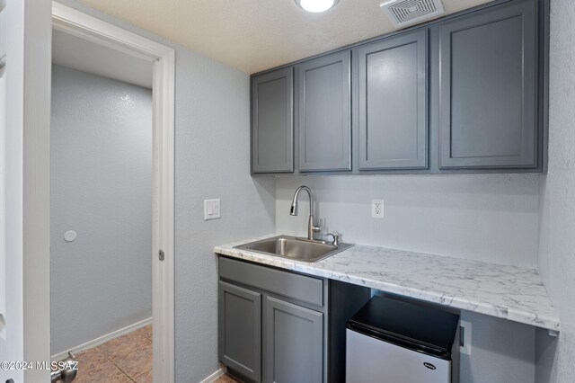 kitchen with light tile patterned flooring, sink, gray cabinets, and white fridge