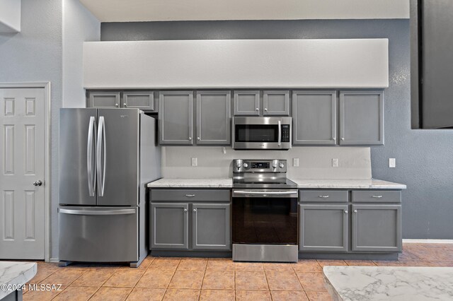 kitchen with light stone counters, gray cabinets, appliances with stainless steel finishes, and light tile patterned floors