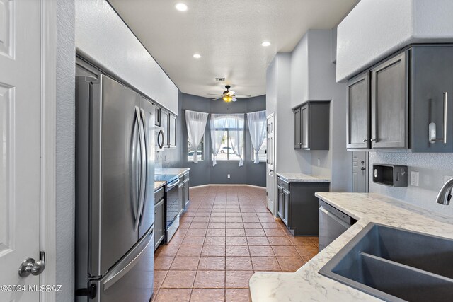 kitchen featuring gray cabinetry, light stone counters, stainless steel appliances, ceiling fan, and sink