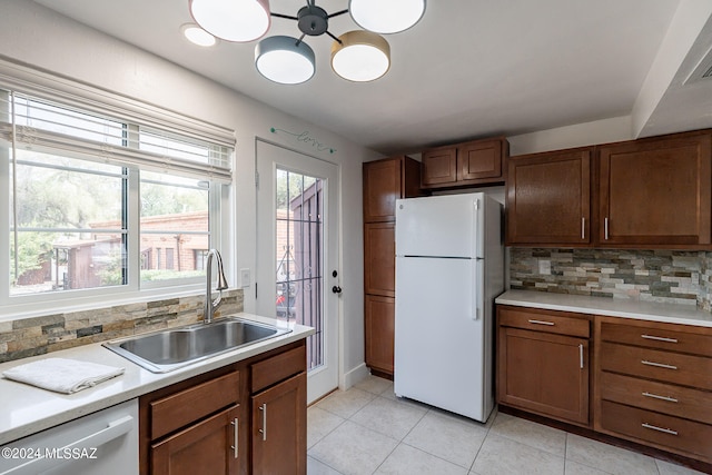 kitchen featuring tasteful backsplash, sink, an inviting chandelier, white appliances, and light tile patterned floors