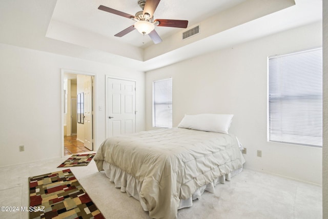 bedroom with light colored carpet, ceiling fan, and a raised ceiling