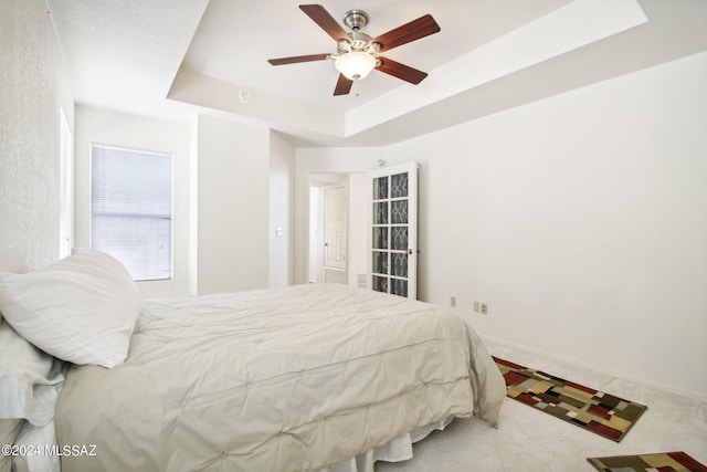 bedroom with ceiling fan, a tray ceiling, and carpet