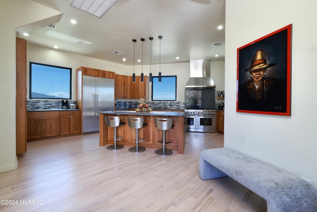 kitchen featuring decorative light fixtures, wall chimney exhaust hood, light hardwood / wood-style floors, high quality appliances, and a center island