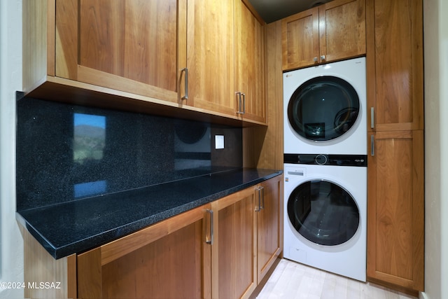 clothes washing area with stacked washing maching and dryer, light hardwood / wood-style floors, and cabinets