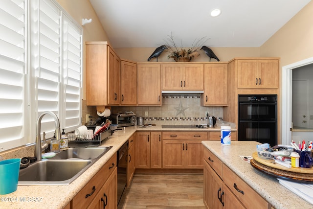 kitchen with light stone counters, light hardwood / wood-style floors, sink, black appliances, and decorative backsplash