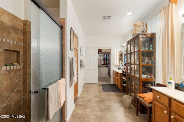 bathroom with tile patterned flooring, a tile shower, and vanity