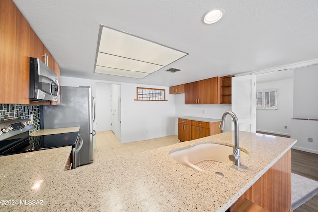 kitchen with kitchen peninsula, light stone countertops, sink, and range