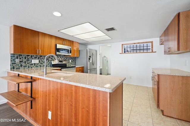 kitchen with sink, light tile patterned floors, light stone countertops, appliances with stainless steel finishes, and kitchen peninsula