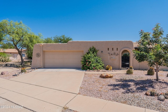 pueblo revival-style home with an attached garage, stucco siding, and concrete driveway