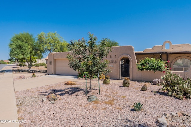 pueblo revival-style home with an attached garage, concrete driveway, and stucco siding