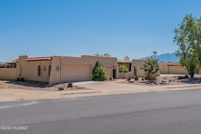 pueblo-style home featuring a mountain view, an attached garage, driveway, and stucco siding