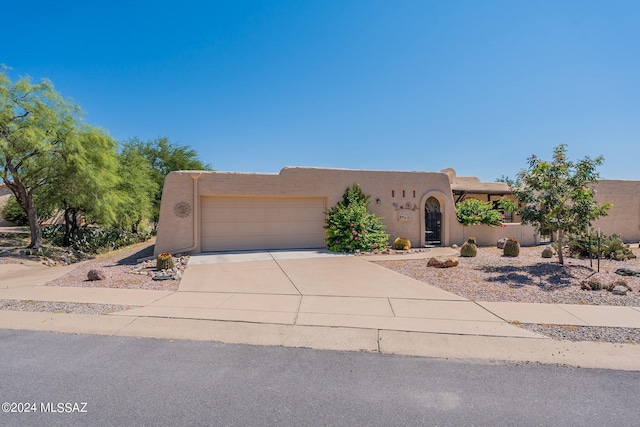 pueblo revival-style home featuring a garage, stucco siding, and concrete driveway
