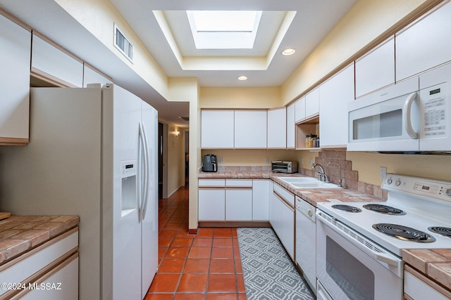 kitchen with sink, white appliances, white cabinetry, a skylight, and tile counters